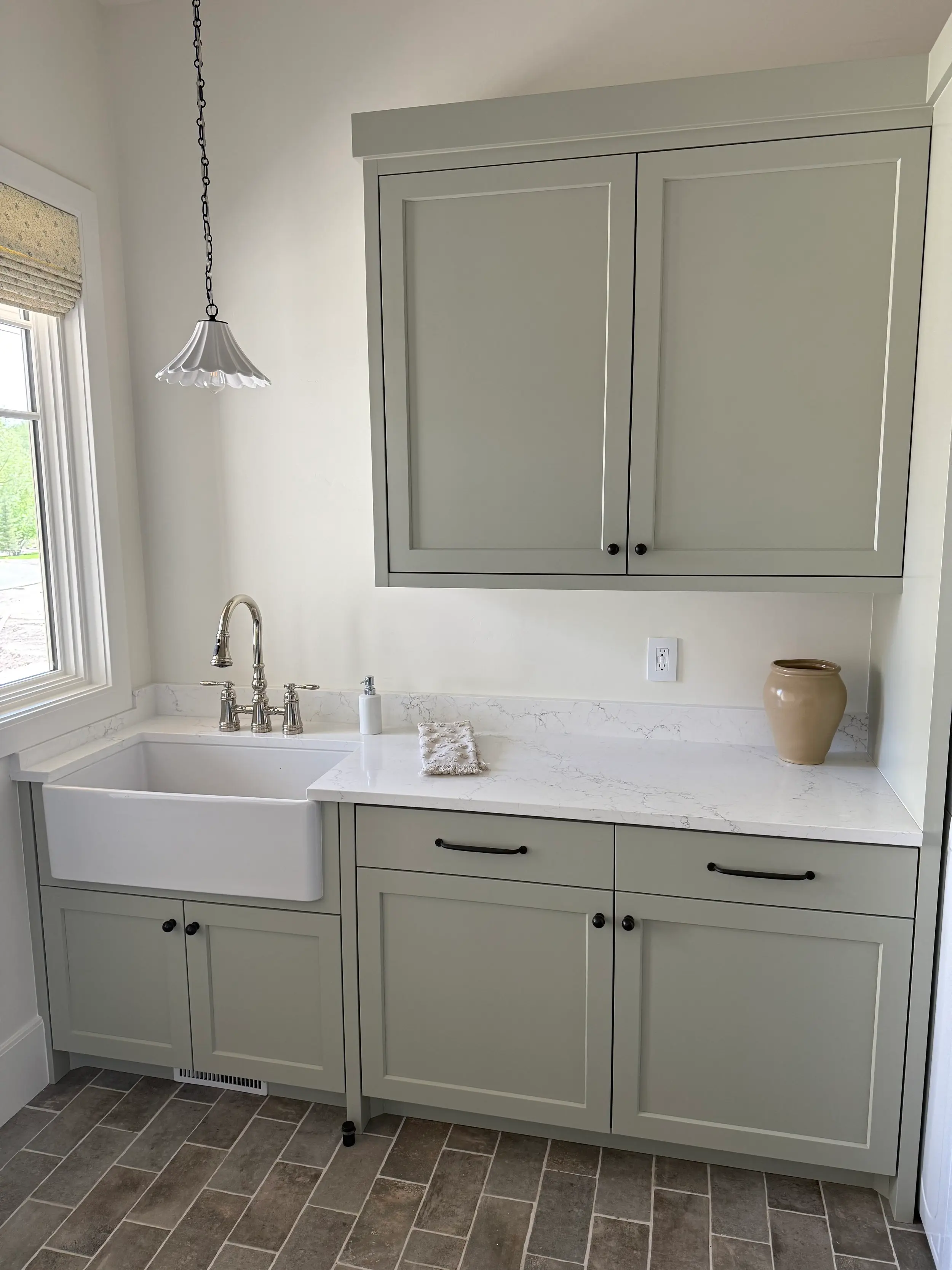 Custom laundry room cabinetry surrounding a farmhouse sink, built in sage green shaker style with quartz countertop and brass fixtures.