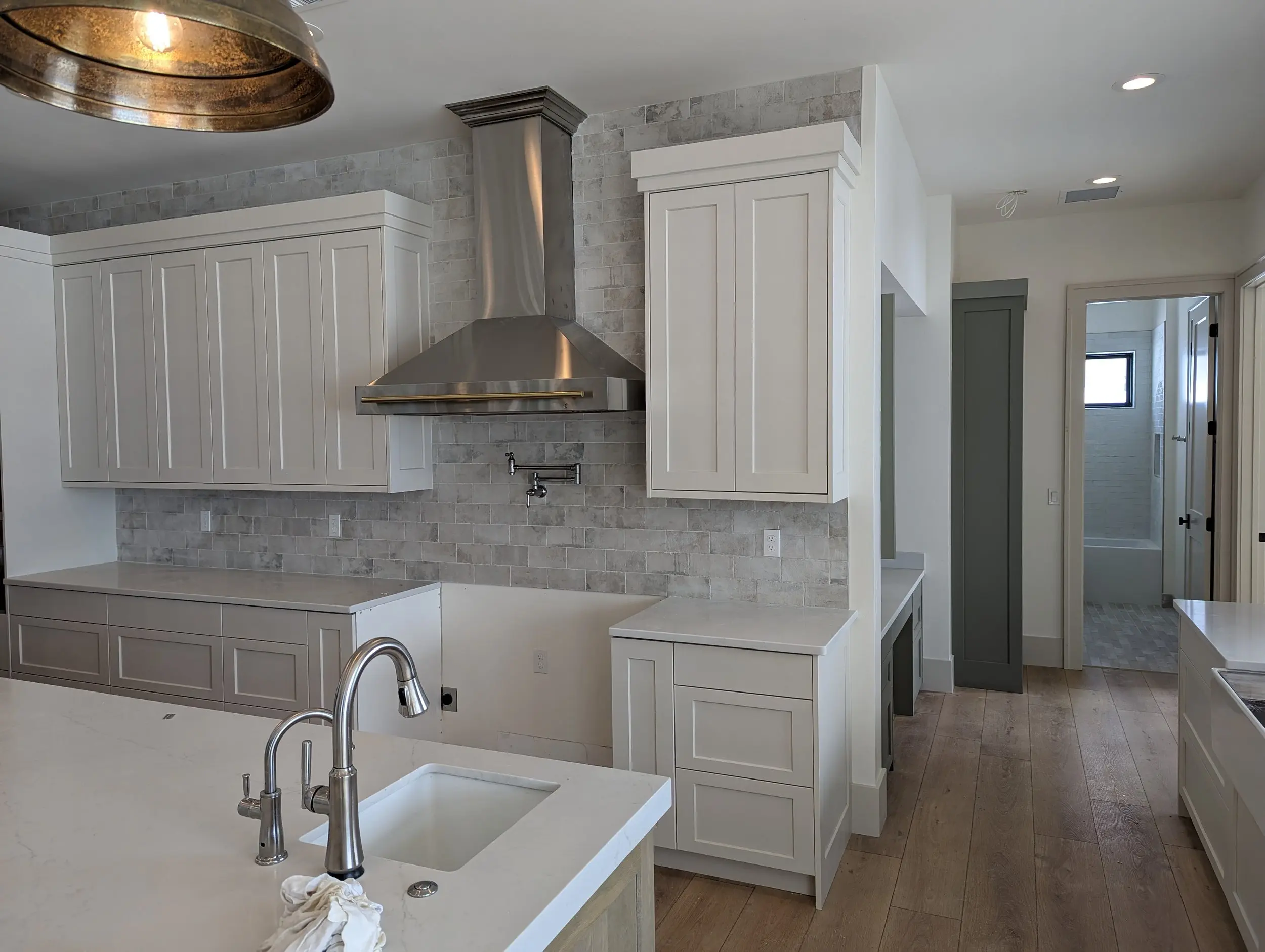 Custom white shaker kitchen island with hand-finished stone backsplash and layered pendant lighting, built by a fine cabinetry shop.